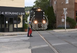 A train travels through downtown Dover, NJ while a flag man stops traffic.