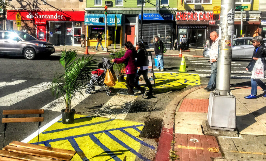 A woman pushing a stroller and other people walk through a demonstration project in Jersey City, showing how curb bump outs could improve the crossing experience.