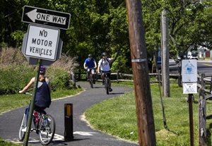 Bicyclists travel along Keyport Trail in Monmouth County with One Way and No Motor Vehicles signs in foreground