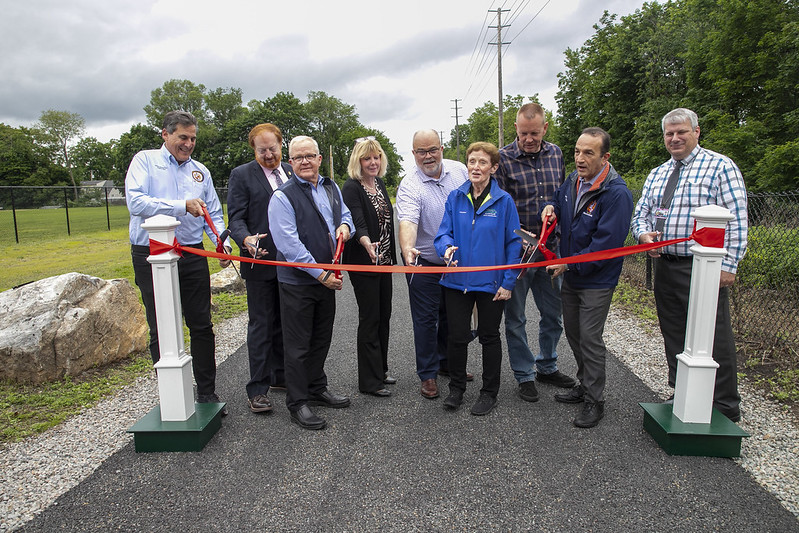 Nine people lined up across Pompton Valley Rail Trail for ribbon cutting.