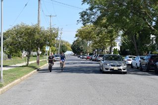 Bikes travel along street in Belmar as car passes them.