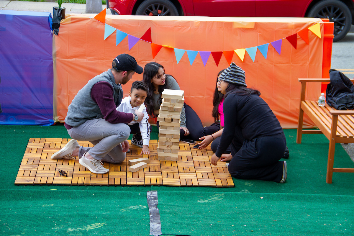 Two adults and three children play Jenga-style game in parklet