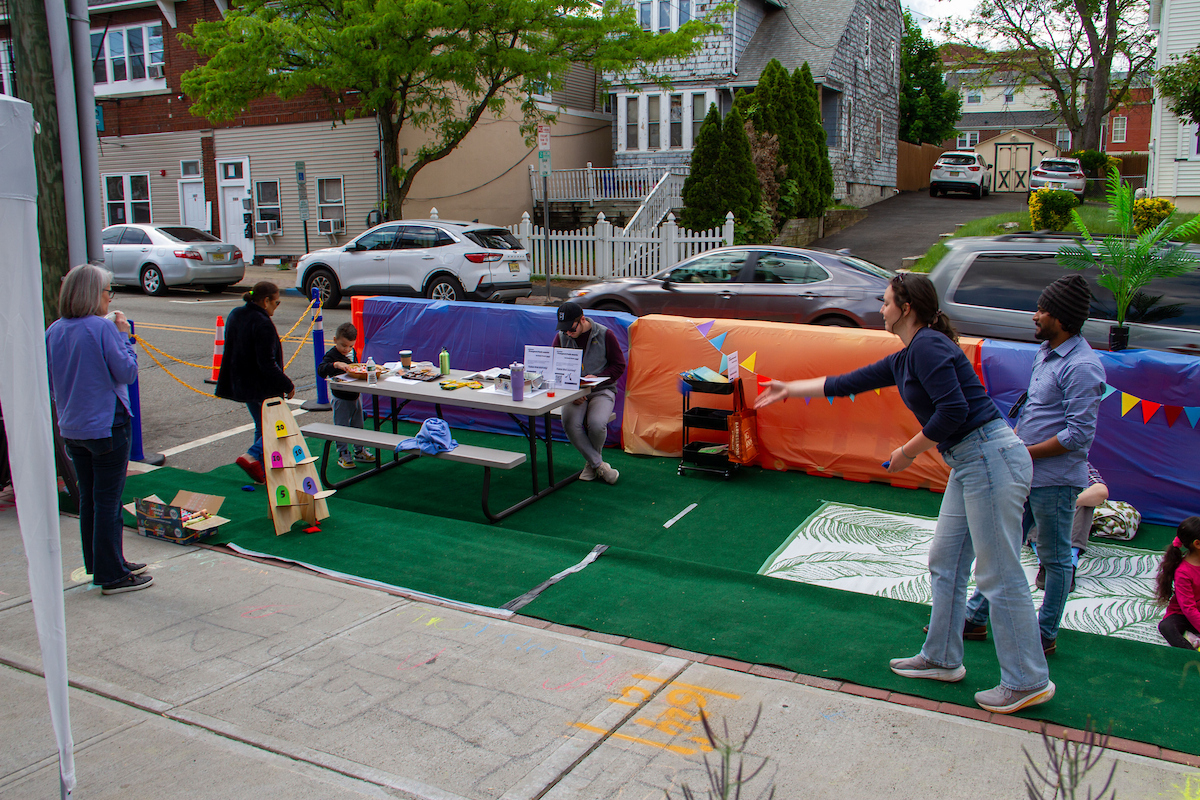 Two people play cornhole-like game, tossing items from right to left in parklet