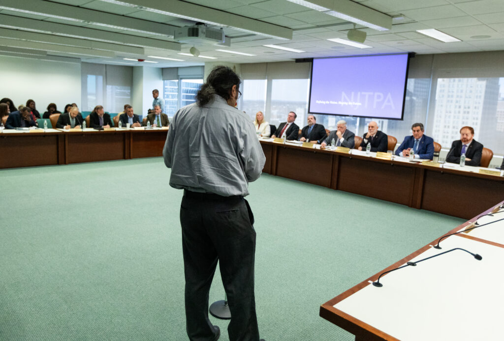 A man stands at a microphone and addresses the NJTPA Board of Trustees.