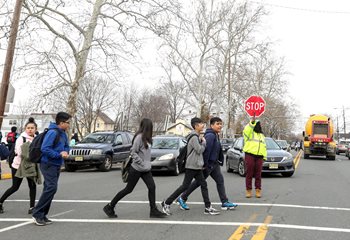 A crossing guard holds up a stop sign to stop cars while children cross the street.