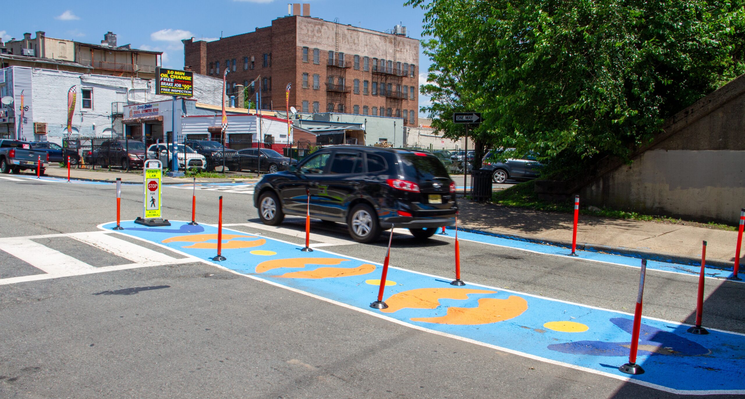 Car travels through crosswalk amid delineators and colorfully painted median