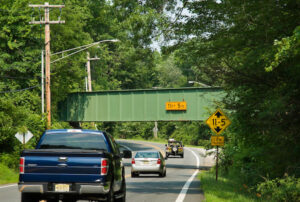 Vehicles traveling on Berkshire Valley Road pass under railroad bridge with low clearance signs of 11 feet, 5 inches.