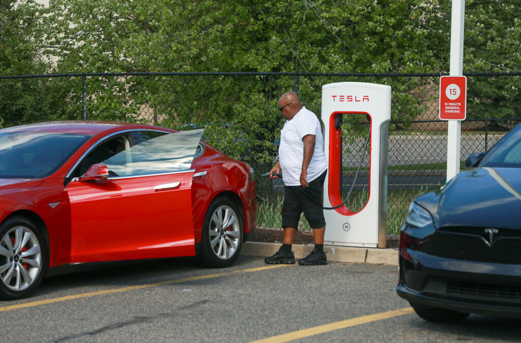 Man prepares to charge Tesla at electric vehicle charging port in Flemington