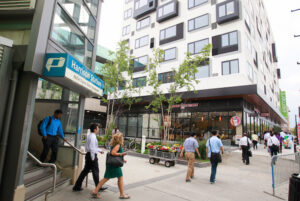 Commuters file out of stairwell at Harrison PATH station amid residential buildings.