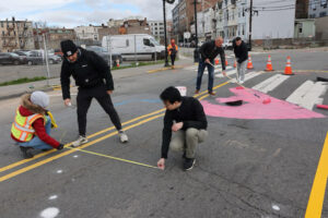People measure and paint around Monticello Avenue in Jersey City as part of traffic-calming initiative.