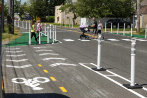 People cross in crosswalk near bollards and painted corner.