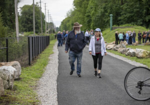 Couple walks along Pompton Valley Rail Trail with people in background.