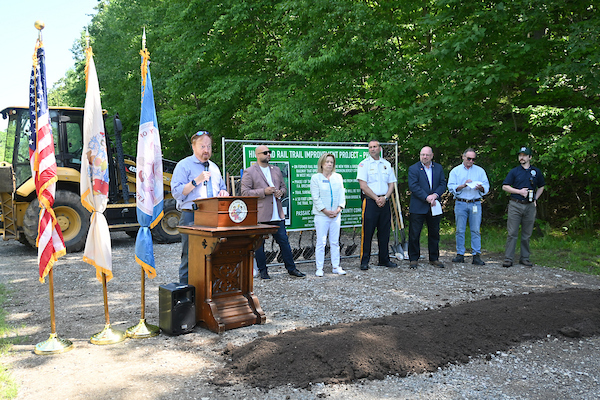 Commissioner John Bartlett speaks at podium of groundbreaking for Highlands Rail Trail Phase II with officials behind him.