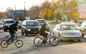 Two people on bicycles cross Route 202 in Hunterdon County as vehicle traffic waits at light.