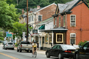 Person on bicycle rides through downtown in Hunterdon County along storefronts, parked cars.