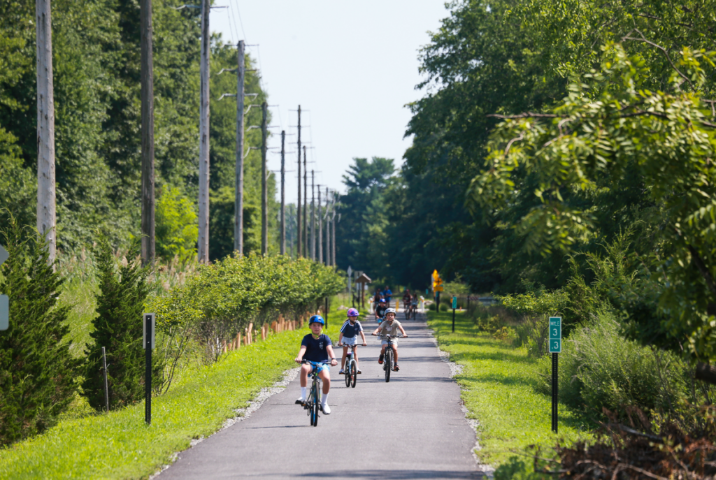 Kids on bikes in distance biking along paved multi-use path, Pompton Valley Rail Trail.